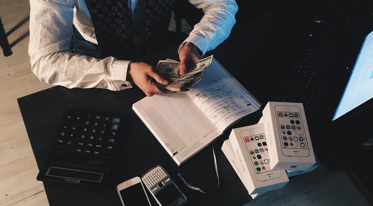 Businessman organizing finances with tech devices and cash on desk.